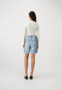 Lys blå denimshorts med frynset kant, baklommer og et lite merke; kombinert med en tettsittende hvit langermet topp.