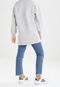 Felpa grigia a maniche lunghe con orlo arrotondato, abbinata a jeans chiari con orlo sfilacciato e scarpe sportive bianche e nere.