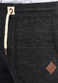 Joggers grises texturizados con cintura ajustable y cordón en color crema. Presentan un parche de cuero marrón con forma de diamante y detalle del logo.