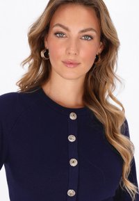 Cardigan navy con scollatura rotonda, caratterizzato da cinque bottoni argentati lucidi lungo la parte anteriore e una superficie a maglia liscia.