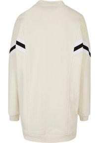 Krämfärgad sweatshirt med svarta och vita randiga detaljer på ärmarna, ribbade muddar och en rund halsringning. Mjuk tygtextur.