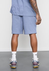 Light blue cotton shorts with a relaxed fit and visible seams. Paired with white socks and gray-purple running shoes.