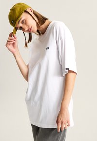 Hvid oversized T-shirt med et lille sort "VANS" logo på brystet. Sæt sammen med en sennepsgul cap med en buet skygge.