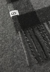 Gray wool scarf with a patterned texture, featuring black checkered accents and fringed edges. Includes a small branded white label.