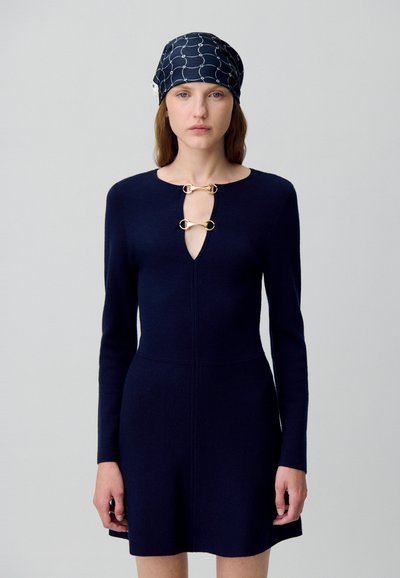 Robe tricotée marine avec un décolleté en clé et des accents en métal doré, dotée de manches longues. Accompagnée d'un foulard assorti à motif.