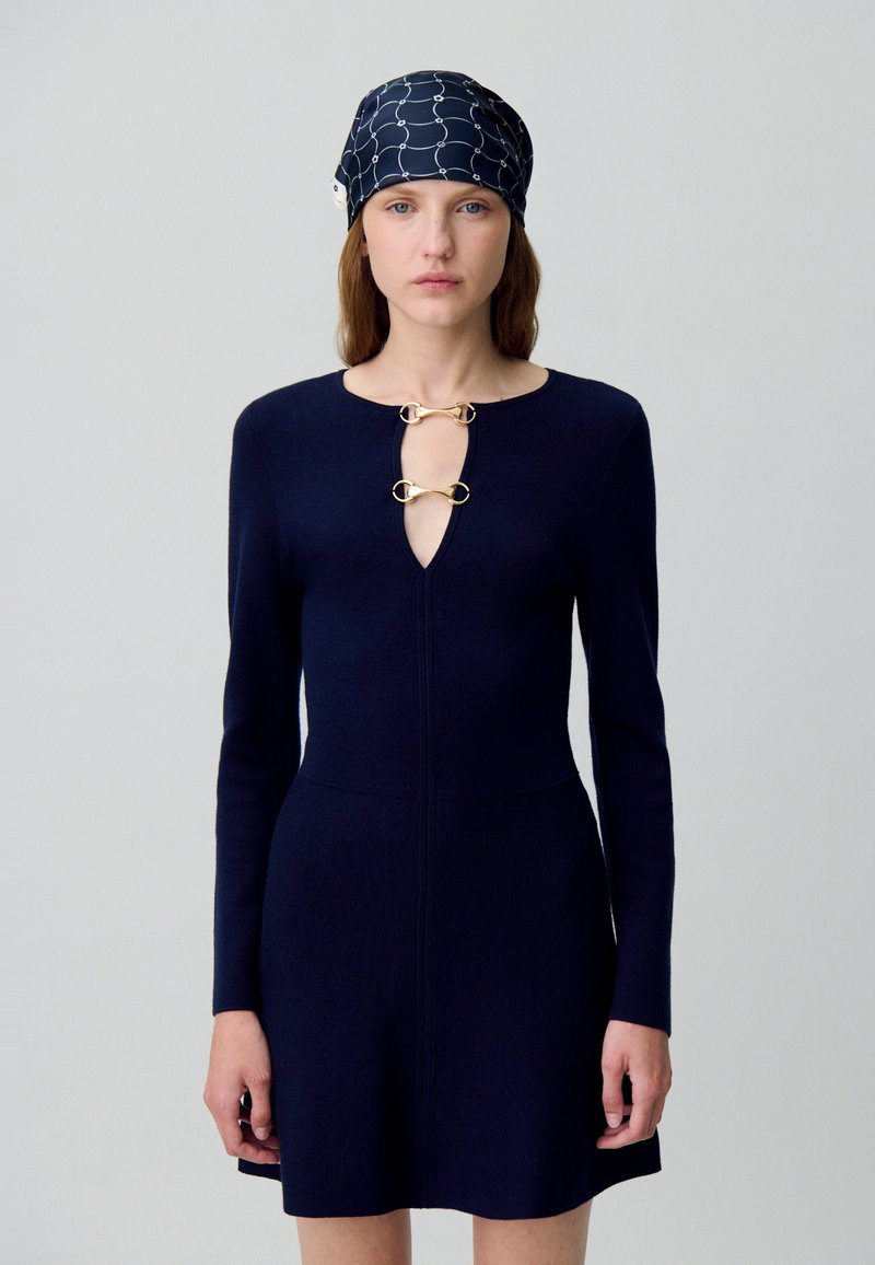 Abito in maglia blu navy con scollatura a chiave e dettagli in metallo dorato, maniche lunghe. Accompagnato da un fazzoletto per la testa abbinato con motivo.