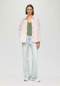 Lichtroze button-up jack over een groene top, gecombineerd met lichtblauwe distressed jeans en witte sneakers. Gladde stof met een relaxed fit.