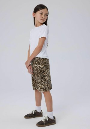 Camiseta blanca de manga corta combinada con pantalones cortos hasta la rodilla con un patrón de leopardo en tonos marrón y beige. Zapatillas marrones y calcetines blancos.