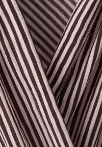 Gros plan d’un tissu rayé marron et blanc avec des coutures visibles et des plis créant un motif texturé.