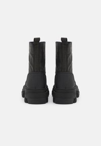 Botas negras hasta el tobillo con un exterior de cuero texturizado y suela de goma. Presentan tiradores y un tacón grueso para mayor soporte.