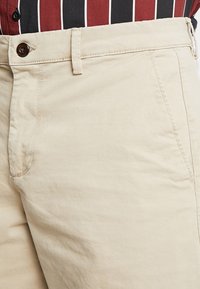 Beige katoenen broeken met een rechte pasvorm, voorkruiden, en een knoopsluiting aan de taille met subtiele stikdetails.