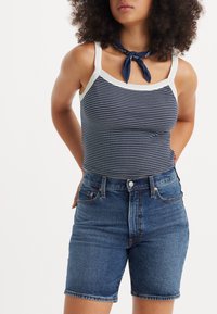 Navy a bíle pruhovaný top na ramínka se širokými ramínky, kombinovaný s modrými džínovými šortkami s vysokým pasem. Hladký materiál, přiléhavý střih a klasický design.