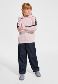 Lichtroze hoodie met zwarte accenten op de mouwen, gecombineerd met donkerblauwe baggy jeans en blauwe sportschoenen.