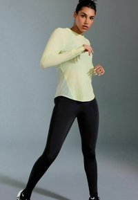 Kergekaaluline, pikakäiselne, neoonkollane spordijakk, millele on sobitatud mustad, modelleeritud retuusid. Sile tekstuur, ergonoomiline disain liikumiseks.