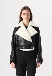 Sort læder cropped jakke med hvidt shearling krave og manchetter, med bæltestil og brede klapper, præsenteret på en neutral baggrund.