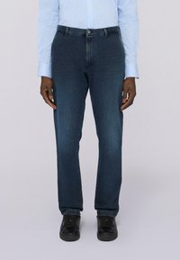 Vaqueros de mezclilla azul oscuro con un diseño de pierna recta, que cuentan con un cierre de botón y costuras sutiles. Combinados con zapatos negros.