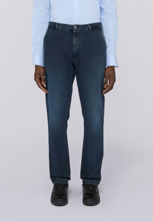Dunkelblaue Denim-Jeans mit geradem Schnitt, ausgestattet mit einem Knopfverschluss und dezenten Nähten. Kombiniert mit schwarzen Schuhen.