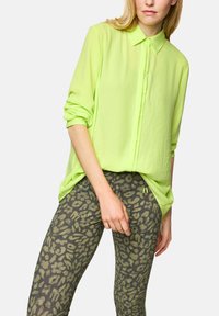 Light green button-up shirt with long sleeves paired with dark green leggings featuring a textured leopard print pattern.