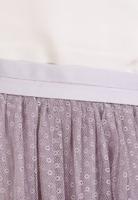 Haut en tissu blanc avec une taille élastique lilas, sur une jupe en tulle lilas superposée avec un motif à pois.