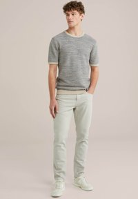 Camiseta de punto a rayas gris claro con cuello redondo, combinada con pantalones ajustados beige claro y zapatillas blancas. Textura suave y diseño casual.