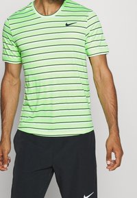 Camisa de manga corta a rayas verdes con líneas horizontales negras, cuello redondo y un pequeño logo negro de Nike en el pecho. Textura suave.