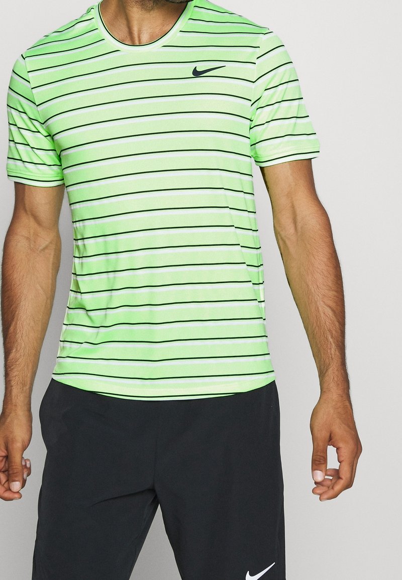 Camisa de manga corta a rayas verdes con líneas horizontales negras, cuello redondo y un pequeño logo negro de Nike en el pecho. Textura suave.