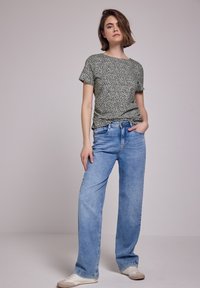 Top a maniche corte bianco e nero a fantasia abbinato a jeans a gamba larga blu chiaro, completato da sneakers bianche.