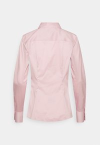 Camicia rosa sartoriale con colletto, maniche lunghe e design aderente. Texture liscia e linee pulite ne valorizzano la silhouette strutturata.