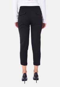 Pantaloni neri a tre quarti con una texture liscia, con risvolti e due tasche posteriori. Abbinati a scarpe nere con tacco alto.