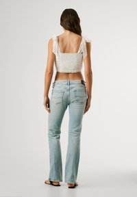 Valkoinen lyhyt toppi, jossa on pitsiyksityiskohtia ja solmittavat hihnat, yhdistettynä vaaleansinisiin väljälahkeisiin farkkuihin. Sileä tekstuuri, rento istuvuus, minimalistinen muotoilu.