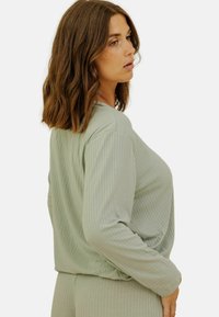 Top long à manches longues rayé vert clair, à coupe décontractée et col rond, avec un tissu texturé et un léger fronce à l'ourlet.