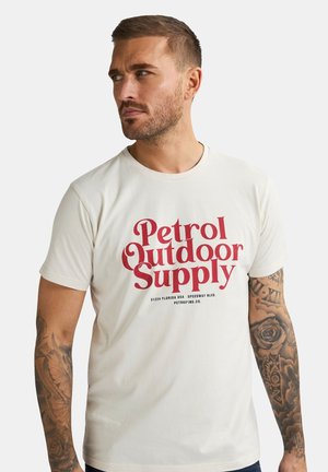 Crème-kleurig t-shirt met vetgedrukte rode tekst "Petrol Outdoor Supply" en kleinere details eronder. Gemaakt van zachte stof met een klassieke pasvorm.