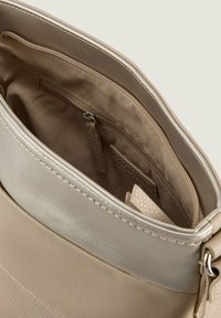 Beige Handtasche mit einer großen Öffnung, ausgestattet mit einer glatten, glänzenden Oberfläche und einem Stofffutter. Enthält eine Reißverschlusstasche und strukturierte Akzente.