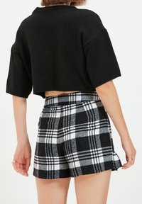 Maglione corto nero con maniche corte e larghe abbinato a pantaloni shorts a quadri bianchi e neri con un leggero orlo arricciato.