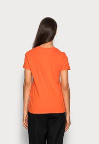 Camiseta corta de manga corta en color naranja con un cuello redondo clásico, textura suave y un diseño ajustado, expuesta desde la parte de atrás.