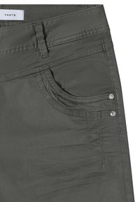 Pantalones gris oscuro de cerca mostrando el bolsillo delantero, la trabilla del cinturón, doble costura y dos remaches metálicos cerca del borde del bolsillo.