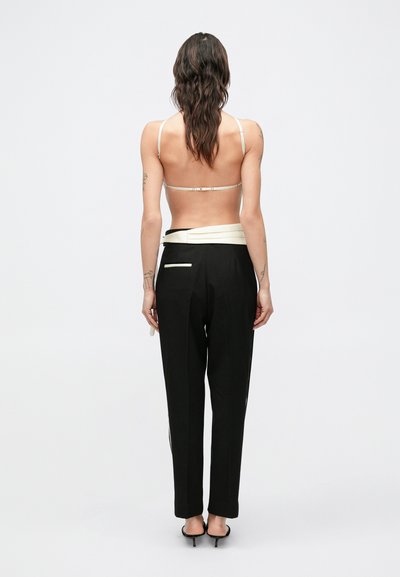 Čierne nohavice na mieru s krémovým opaskom, s jedným zadným vreckom a rovnými nohavicami. Modelka nosí jednoduchý top so strapcami.