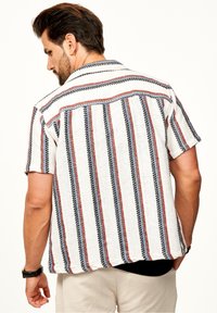 Kurzärmeliges, kragenloses Hemd mit lockerer Passform. Weiße Grundfarbe mit roten und blauen vertikalen Streifen, aus strukturierter Stoffe und mit kontrastierenden Nähten.