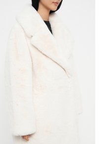 Hvid, fluffy oversized frakke med bred klappeskrave, blød tekstur og lige ærmer. Stoffet ser varmt og hyggeligt ud.