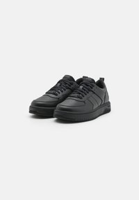 Sneaker nere con finitura in pelle liscia, punta perforata e cuciture a contrasto. Presentano lacci piatti e una suola in gomma testurizzata.