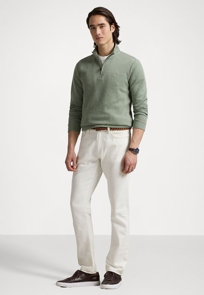 Green knit quarter-zip sweater, white pants, dark brown shoes. Sweater has ribbed cuffs and a logo on the chest. Rope belt adds detail.