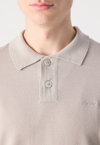Beige pikétröja i texturerad tyg med klassisk krage, tvåknapps placket och broderad "BOSS"-logotyp på bröstet.