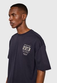 Marinblå bomullst-shirt med tryckt motiv på bröstet med text och siffror. Avslappnad passform med korta ärmar och rund hals.