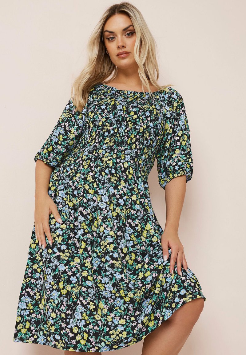 Blumenkleid mit schwarzem Grund, das ein Muster aus blauen und gelben Blumen zeigt, mit kurzen Ärmeln, einem lockeren Schnitt und einem gerafften Oberteil.