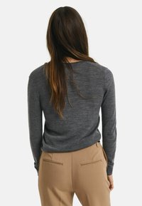 Pull en tricot gris à manches longues, col rond et texture lisse, associé à un pantalon beige ajusté avec poches passepoilées.