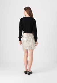 Svart cropped genser og et miniskjørt med sølvfring. Skjørtet har skinnende, lagdelte fringer, mens genseren har lange ermer og rund hals.