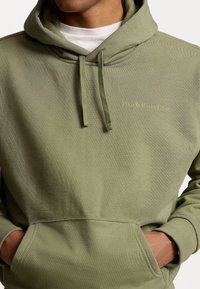 Olivově zelená mikina s kapucí vyrobená z měkké tkaniny, s přední kapsou, šňůrkovou kapucí a zlatým logem "Polo Ralph Lauren" na hrudi.