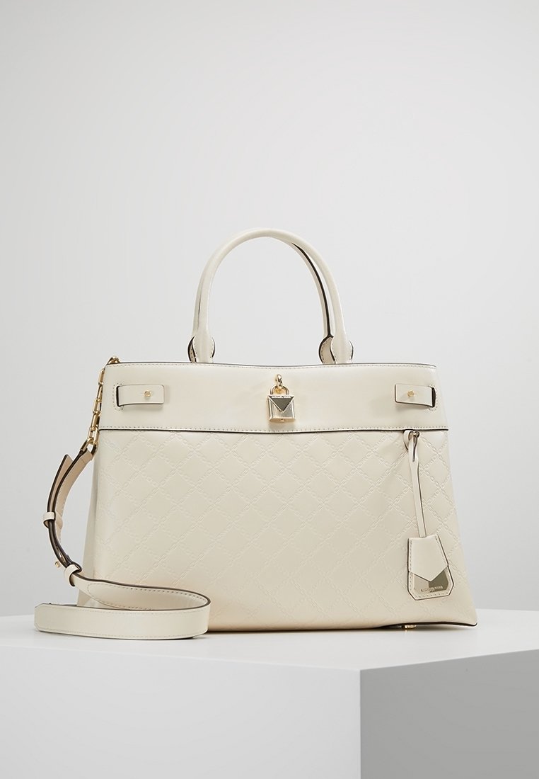 Sac à main en cuir matelassé crème avec poignées supérieures, bandoulière amovible, détail de serrure dorée et étiquette de marque sur le côté.