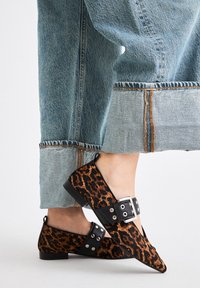 Zapatos planos de estampado de leopardo con puntas afiladas, correas negras con hebillas plateadas, combinados con pantalones de mezclilla azul con dobladillos deshilachados.