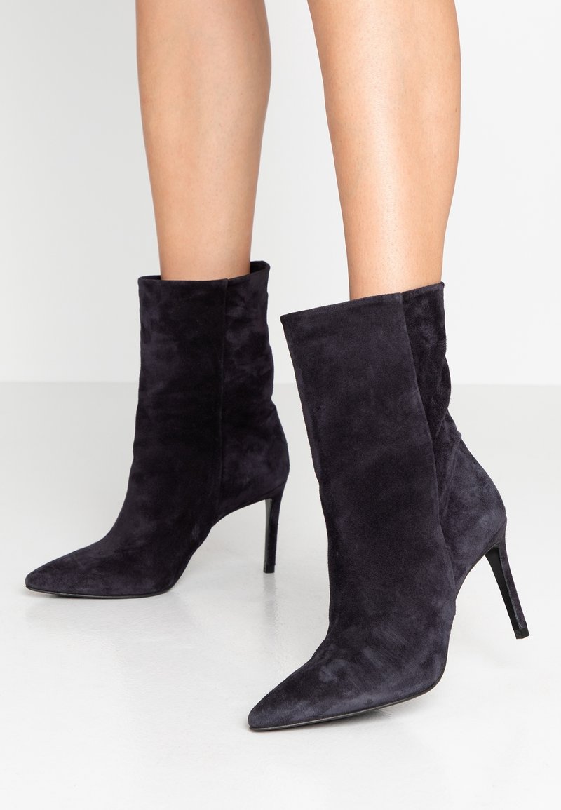 Bottines en suède noir avec un bout pointu et un talon haut élancé. Le design est élégant avec une texture lisse et simple, sans embellissements visibles.